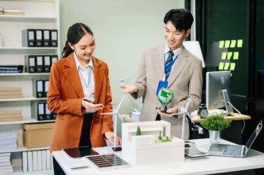 Masanın yanında duran bir grup iş adamı konut projesinden alınan bina modeline bakıyor. Yeşil iş şirketi ve Güneş Enerjisi Çevre Kenti Kavramı.