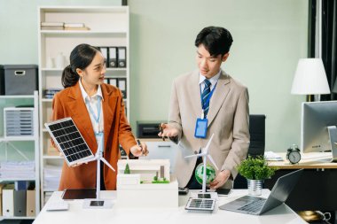 Masanın yanında duran bir grup iş adamı konut projesinden alınan bina modeline bakıyor. Yeşil iş şirketi ve Güneş Enerjisi Çevre Kenti Kavramı.