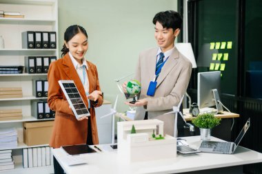 Masanın yanında duran bir grup iş adamı konut projesinden alınan bina modeline bakıyor. Yeşil iş şirketi ve Güneş Enerjisi Çevre Kenti Kavramı.