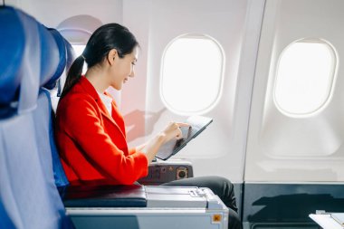 Çekici Asyalı kadın uçak yolcusu tablet kullanırken rahat koltukta oturuyor.