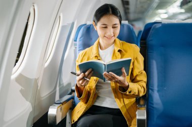Çekici Asyalı kadın uçak yolcusu rahat koltukta oturuyor ve deftere yazıyor. 