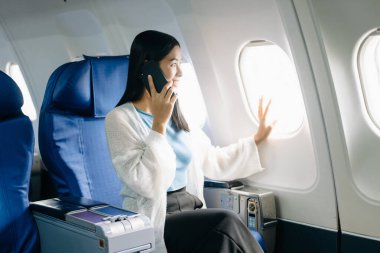 Uçakta birinci sınıfta telefonla konuşan genç Asyalı kadın.  