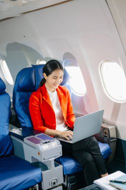 Çekici Asyalı kadın uçak yolcusu dizüstü bilgisayarla çalışırken rahat koltukta oturuyor.