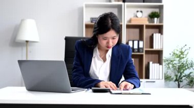 İş kadını masada oturuyor, ofiste çalışıyor ve hesap makinesiyle dizüstü bilgisayar kullanıyor. 