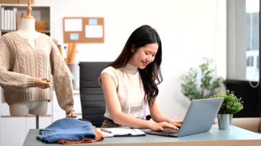 Başarılı bir moda tasarımcısı. Atölyede çalışırken gülümseyen çekici bir kadın. Stüdyoda dizüstü bilgisayar kullanan güzel bir kadın.