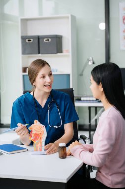 Beyaz kadın doktor klinikteki Asyalı kadın hastayla semptomları tartışıyor.