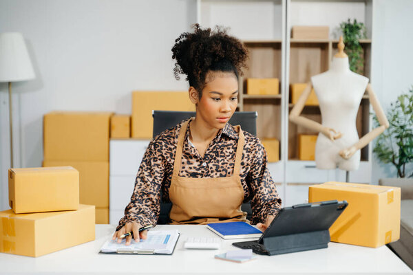 Владелец афроамериканского предпринимателя женщина готовит упаковку продуктов коробки для покупок онлайн заказов. Концепция запуска малого бизнеса.