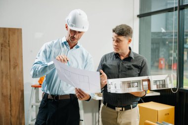 Mimaride profesyonel işbirliği. İki mühendis, dizüstü bilgisayarlar, tabletler ve ölçekli modeller gibi araçlar kullanarak inşaat planları üzerinde çalışıyor..