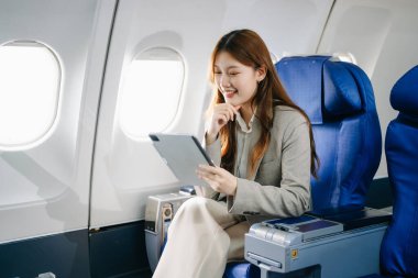 Genç Asyalı iş kadını dijital tabletle uçakta birinci sınıfta. 