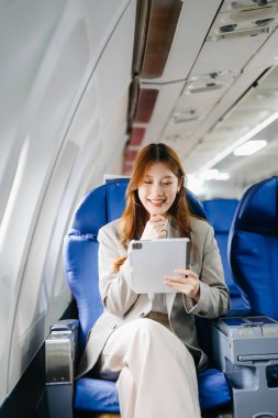 Genç Asyalı iş kadını dijital tabletle uçakta birinci sınıfta.  