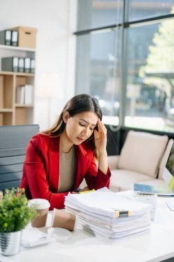 Çok çalışan Asyalı genç işkadını ofis çalışanı ofis masasında uzun bir gün geçirdikten sonra baş ağrısından muzdarip. ofis sendromu kavramı 