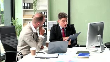 İki iş adamı iş hakkında konuşuyor ve ofiste bilgisayar kullanıyor. 