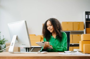 Başlangıçta küçük işletme KOBİ 'si, bilgisayar ve dijital tablet kullanan girişimci kadın paket ürün kutularını hazırlamak için çevrimiçi satın alma siparişini alır ve kontrol eder