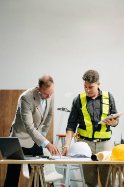 Müteahhit ve mimar planı tablet, dizüstü bilgisayar kullanarak ve büyük bir proje üzerinde çalışmakla ilgili konuşarak ele alıyorlar. İnşaat sürecinde bina içi