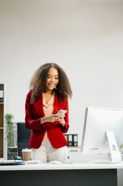 Yaratıcı ofiste akıllı telefon ve bilgisayar üzerinde çalışan kendine güvenen bir iş kadını. 