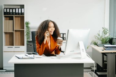 Akıllı telefondan konuşan kendine güvenen iş kadını yaratıcı ofiste bilgisayarla çalışıyor.