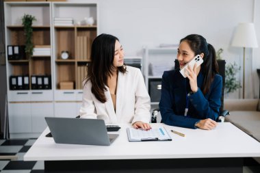 Genç iş adamları yeni bir proje üzerinde çalışıyor. Proje yöneticileri dizüstü bilgisayarla toplantı yapıyor ve akıllı telefondan konuşuyor  