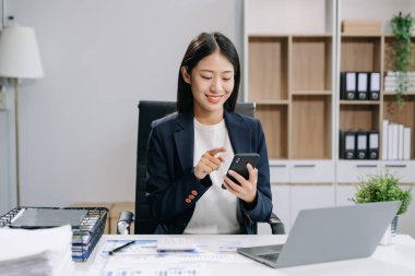 İş yerinde otururken akıllı telefon ve dizüstü bilgisayar kullanan genç ve güzel bir iş kadını. İşine odaklan..   