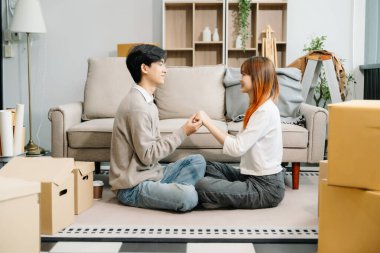 Kutuları olan mutlu Asyalı genç çift yeni bir eve taşınıyor. El ele tutuşarak yerde oturuyorlar. 