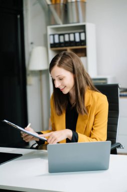 İş kadını, ofis masasında finans raporu hazırlamak için tablet ve laptop kullanıyor.