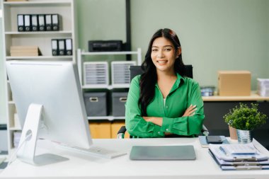 Genç ve çekici Asyalı ofis çalışanı iş kıyafetleri içinde ofiste çalışıyor ve kamerada poz veriyor. 