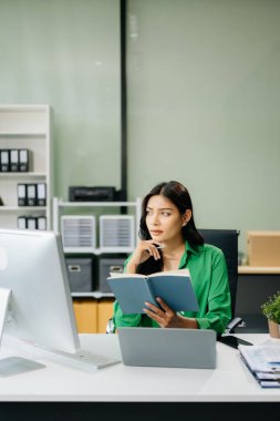 Genç çekici Asyalı kadın ofis çalışanı takım elbiseli ofiste çalışıyor ve kitap okuyor.   