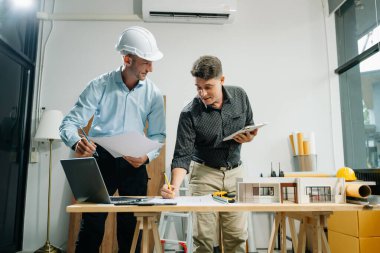 Ofiste mimari tartışan ve dizüstü bilgisayar ve dijital tablet kullanan meslektaşlar