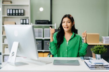 Genç ve çekici Asyalı ofis çalışanı takım elbiseli bilgisayarda çalışıyor ve onayını veriyor.  