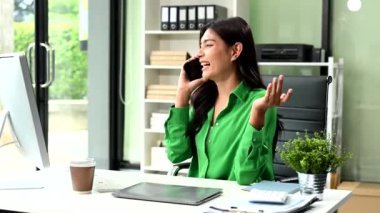 Kendine güvenen iş kadını yaratıcı ofiste bilgisayarla çalışıyor ve akıllı telefondan konuşuyor.