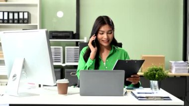 Yaratıcı ofiste dizüstü bilgisayarda çalışan ve akıllı telefondan konuşan kendine güvenen bir iş kadını. 
