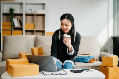  Genç iş kadını internet satışlarını yönetiyor ve modern bir ev ofisinden dizüstü bilgisayar kullanarak ve kahve içerek nakliye yapıyor. 
