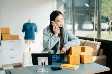 Genç işletme sahibi dijital tabletteki müşterilere internet siparişlerini kontrol ediyor ve akıllı telefondan konuşuyor. Çevrimiçi Alışveriş kavramı.