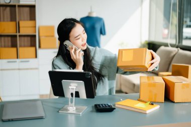 Genç işletme sahibi dijital tabletteki müşterilere internet siparişlerini kontrol ediyor ve akıllı telefondan konuşuyor. Çevrimiçi Alışveriş kavramı.