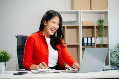 Genç ve çekici Asyalı ofis çalışanı takım elbiseli, ofiste dizüstü bilgisayarla çalışıyor. 