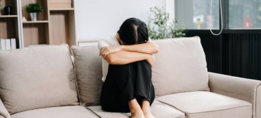 Evdeki kanepede oturan Asyalı kadın depresyonda. 