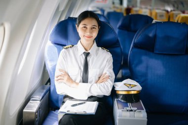 Asyalı, kendine güvenen, üniformalı kadın pilot, uçağın içinde oturuyor.