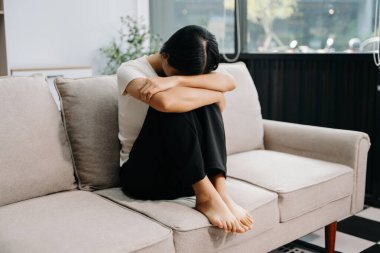 Evdeki kanepede oturan Asyalı kadın depresyonda. 