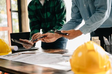 Toplantıdaki mühendis ekibi dijital tablet kullanarak modern şehir modelinin inşaat sahasının planlarıyla birlikte çalışıyor. 