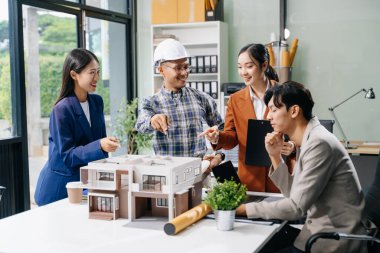 Laptop kullanarak yenilikçi binalar tasarlayan Asyalı profesyonellerle modern bir mimari ofis toplantısını keşfedin. 