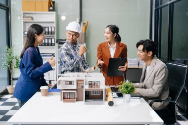 Laptop ve tablet kullanarak yenilikçi binalar tasarlayan Asyalı profesyonellerle modern bir mimari ofis toplantısını keşfedin. 