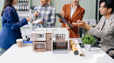 Laptop ve tablet kullanarak yenilikçi binalar tasarlayan Asyalı profesyonellerle modern bir mimari ofis toplantısını keşfedin. 