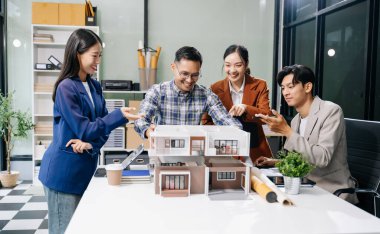 Laptop ve tablet kullanarak yenilikçi binalar tasarlayan Asyalı profesyonellerle modern bir mimari ofis toplantısını keşfedin. 