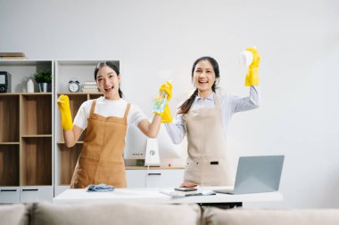 Mutlu Asyalı kadın temizlikçiler oturma odasında verimli ve profesyonel temizlik yapıyorlar.. 