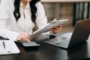 Modern ofiste hesap makinesi, dizüstü bilgisayar ve tablet kullanan bir iş kadınının orta bölümü