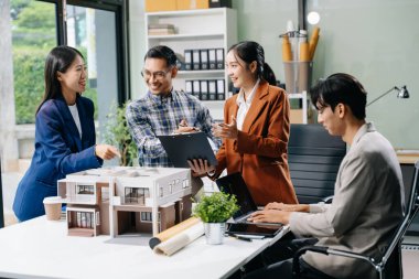 Asyalı mimarlar ve tasarımcılar modern bir ofiste beyin fırtınası yapıyor ve işbirliği yapıyor, modellerden faydalanıyor ve yenilikçi kentsel yapılar tasarlama planları yapıyorlar..