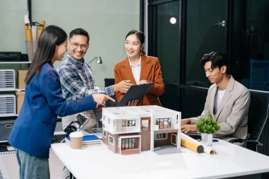 Asyalı mimarlar ve tasarımcılar modern bir ofiste beyin fırtınası yapıyor ve işbirliği yapıyor, modellerden faydalanıyor ve yenilikçi kentsel yapılar tasarlama planları yapıyorlar..