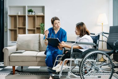 Asyalı genç bayan hemşire tekerlekli sandalyedeki kadın hastaya yardım ediyor. Tıbbi bir ortamda özen, şefkat ve profesyonellik gösterme.