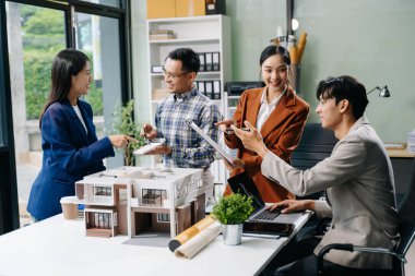 Asyalı mimarlar ve tasarımcılar modern bir ofiste beyin fırtınası yapıyor ve işbirliği yapıyor, modellerden faydalanıyor ve yenilikçi kentsel yapılar tasarlama planları yapıyorlar..