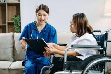 Asyalı genç bayan hemşire tekerlekli sandalyedeki kadın hastaya yardım ediyor. Tıbbi bir ortamda özen, şefkat ve profesyonellik gösterme.