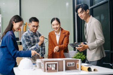 Asyalı mimarlar ve tasarımcılar modern bir ofiste beyin fırtınası yapıyor ve işbirliği yapıyor, modellerden faydalanıyor ve yenilikçi kentsel yapılar tasarlama planları yapıyorlar..